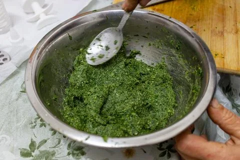 Hand mixing green herb paste in stainless bowl with spoon, close-up, top view. Stock Photos