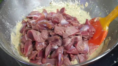 Hand mixing raw chopped chicken gizzards into batter in a metal bowl Video stock 343027132