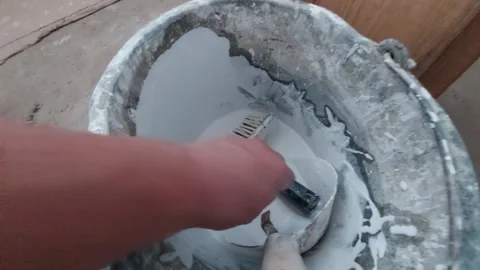 Hand mixing white paint with a brush in a messy construction bucket Vídeos de archivo 336461686
