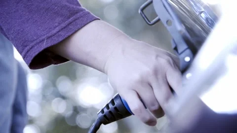 Hand of mom plugging in electric car as her and her toddler walk away in bac Stock Footage 146278274