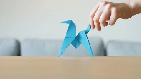 A hand moving a cute stylized blue handmade Origami Horse on a wooden table. Video stock 143810375