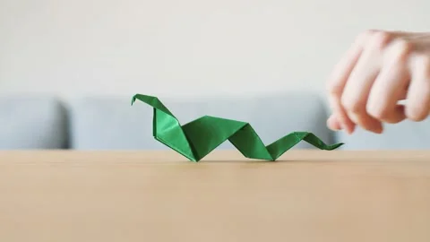 A hand moving a cute stylized green handmade Origami Snake on a wooden table. Stock Footage 143810367