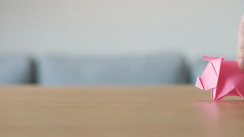 A hand moving a cute stylized pink handmade Origami Pig on a wooden table. Stock Footage 143810312
