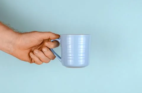 Hand with a mug on a blue background. Stock Photos