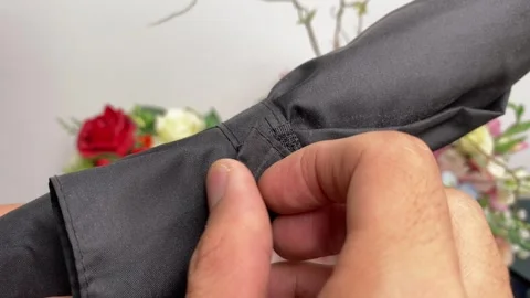 Hand open velcro strap from umbrella. Flower in background Video stock 249788816