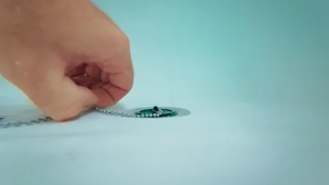 Hand opening bathtub drain by lifting plug on chain for water release, view from Video stock 345125669
