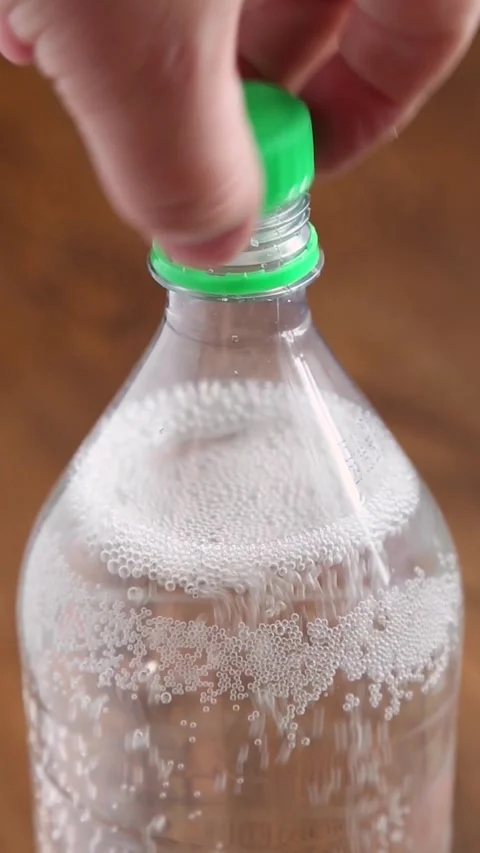 Hand opening green plastic bottle cap revealing carbonated water inside Stock Footage 313260881