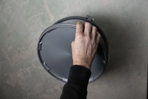 Hand opening plaster or wall filler bucket on concrete floor Stock Photos