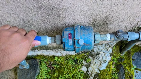Hand opening the valve of a water meter in a moss-covered abandoned place. 4K Stock Footage 324201833