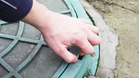 A hand opens a green garden hatch close-up. Water supply well cover Stock Footage 154481348