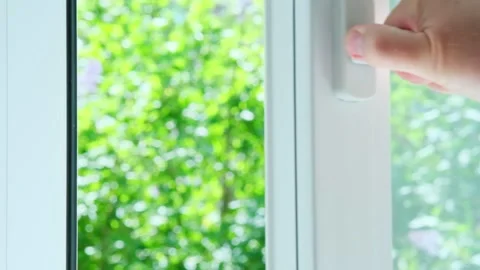 Hand opens handle of white window behind which is beautiful green blurry natural Stockbeeldmateriaal 247018521