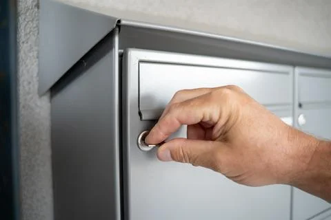Hand opens a mailbox with a key in a row of grey metal mailboxes with drop slots Stock Photos