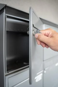 Hand opens a mailbox with a key in a row of grey metal mailboxes Stock Photos