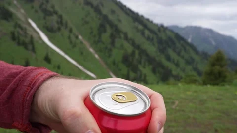 Hand opens soda can outdoors with mountain landscape in background Видео 340391937