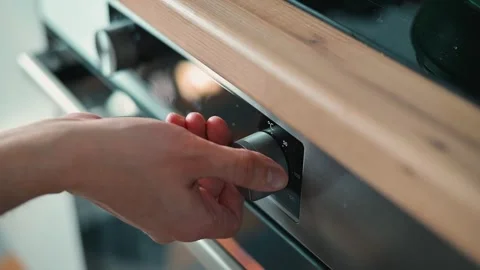A hand operates the temperature dial of an oven in a kitchen setting. This Stock-Footage 338290616