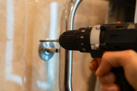 Hand operating a cordless drill to install a metal fixture in a home bathro.. Stock Photos