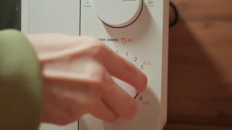 Hand operating microwave rotary knob on white control panel in warm kitchen Stock Footage 343537062