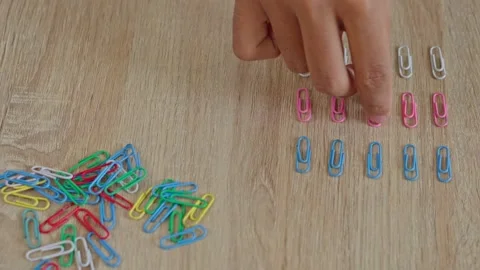 Hand organizing pink, white, and blue paperclips into perfect symmetry on Stock Footage 333501511