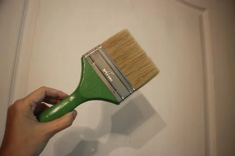 Hand with paintbrush on light wall background. Reconstruction concept Фото