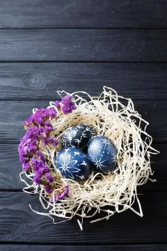Hand painted dark blue easter eggs in nest and flowers on wooden table Stock Photos