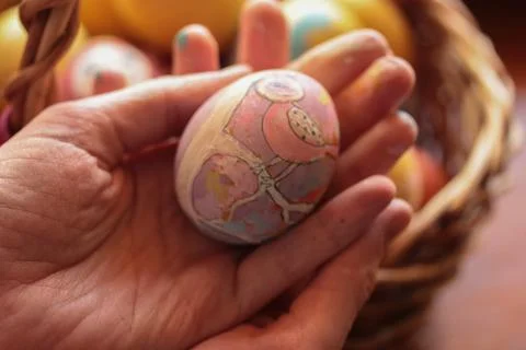 A hand-painted Easter egg in a woman's hands. Warm background. Egg coloring. Stock Photos