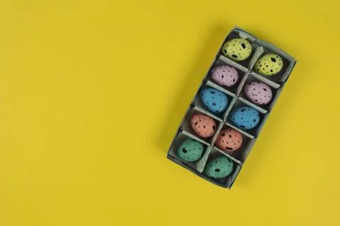 Hand painted Easter quail eggs in carton box isolated on yellow background Stock Photos