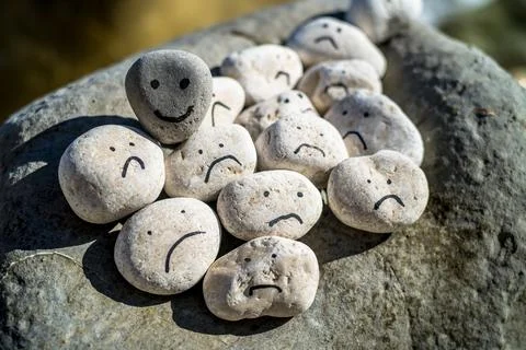 Hand painted smiley face on a small stone. A happy face surrounded by sad faces. Stock Photos
