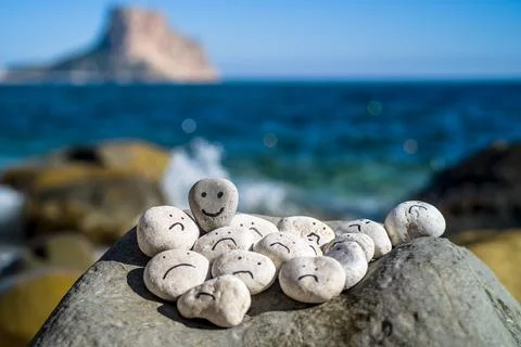 Hand painted smiley face on a small stone. A happy face surrounded by sad faces. Stock Photos