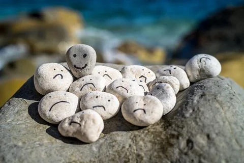 Hand painted smiley face on a small stone. A happy face surrounded by sad faces. Stock Photos