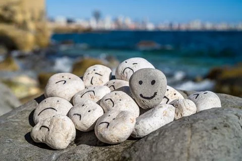 Hand painted smiley face on a small stone. A happy face surrounded by sad faces. Stock Photos