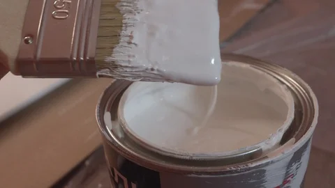 Hand of painter dipping a brush into a bucket with white paint , slow motion Video stock 86017376