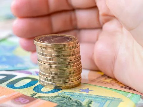 Hand palm protects a stack of coins on euro banknotes cash background. Stock Photos
