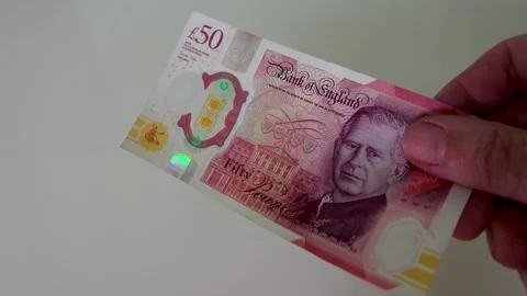 Hand passes a £50 note with King Charles III across frame in slow motion, white Stock Footage 334231270