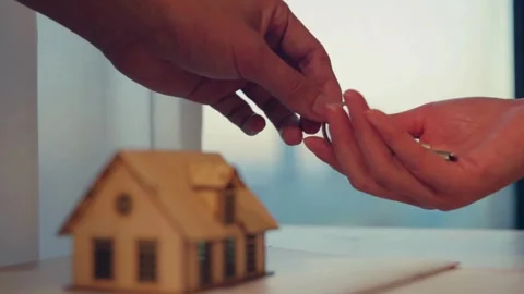 Hand passing house keys over wooden model at sunset Video stock 332279066