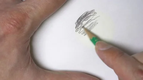 Hand with pencil makes stroke on paper, under which lies dogecoin. Stock Footage 165507110