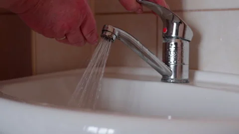 Hand of a person adjusting a modern chrome faucet to control water flow into a Video stock 336067569