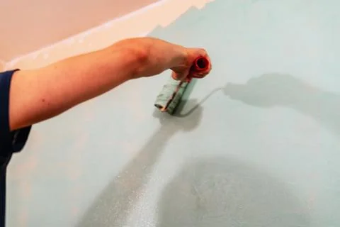 Hand of a person using a paint roller to apply a fresh coat of light blue p.. Stock Photos