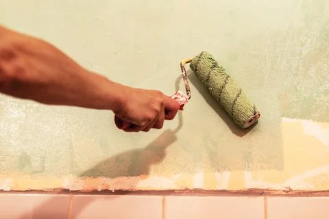 Hand of a person using a paint roller to apply green paint on a wall, showc.. Stock Photos