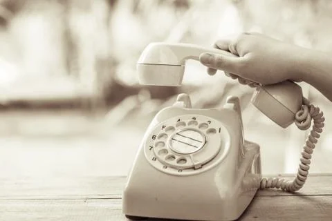 Hand pick up old day phone or rotary telephone on wood table vintage color to Stock Photos