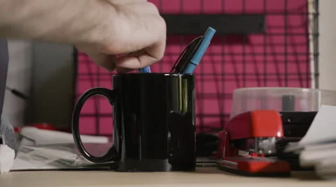 Hand picking up and dropping pens to and from a black mug on a desk Stock Footage 66205554