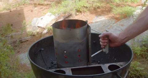 Hand picking up and dumping out red hot charcoal lumps into the smoker port of a Stock Footage 137131532