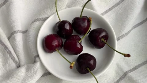 A hand picking up and taking a bite of a fresh dark red cherry Video stock 338186399