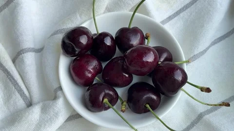 A hand picking up and taking a bite of a fresh dark red cherry Stock Footage 338186400