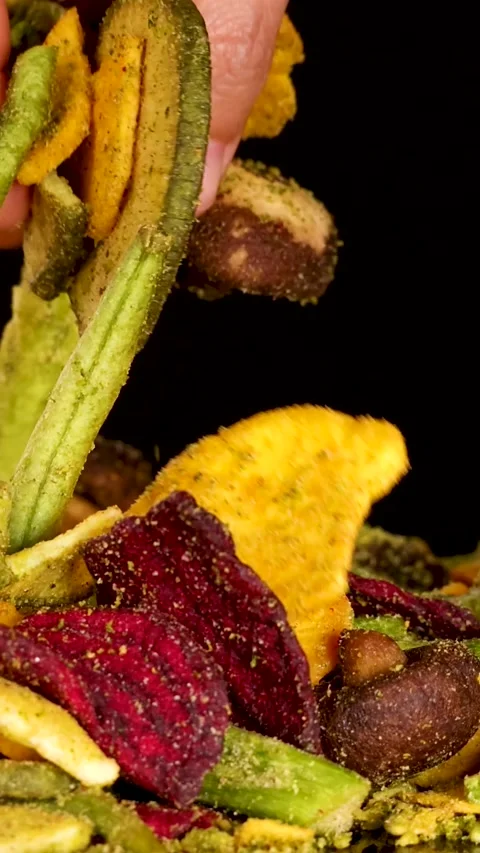 Hand Picking Assorted Dried Vegetable Chips on Black Background Vertical Stock Footage 327272662