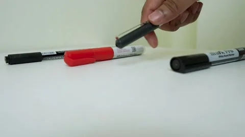 Hand picking up a black marker from a white surface with other markers Stock Footage 318057227