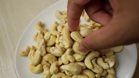 Hand picking cashew nuts from a white plate on a wooden table Stock Footage 318057139