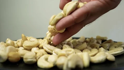 Hand picking cashew nuts from a white plate on a wooden table Stock Footage 318057142
