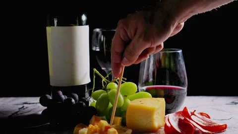 Hand picking cheese from wine and charcuterie board with grapes and red wine Stock Footage 308753763