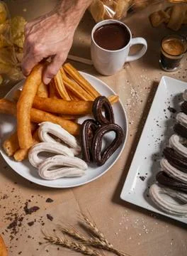 Hand picking up a churro from the table plate with a cup of chocolate. A popu Stock Photos