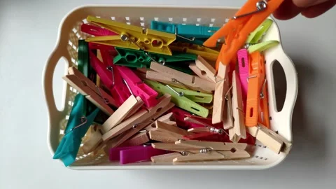Hand Picking Colorful Plastic and Wooden Clothespins from Basket on White Table Stock Footage 337691408